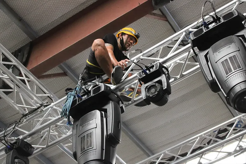 Event technician installing professional lighting equipment on overhead truss